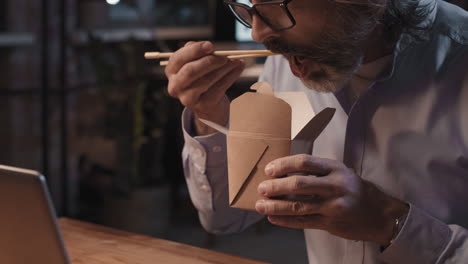 man eating takeout noodles with chopsticks