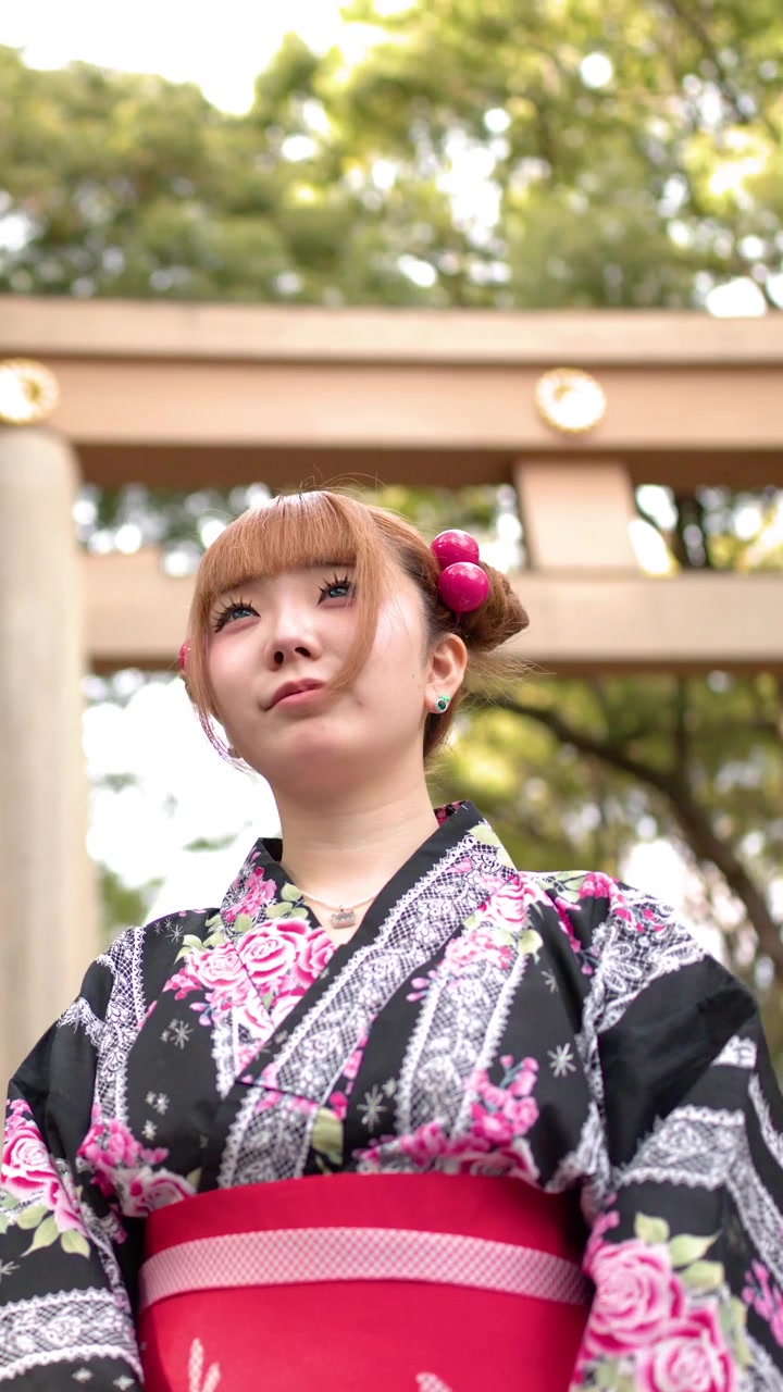 Inquadratura dal basso di una donna in yukata floreale in piedi vicino a un torii di legno.