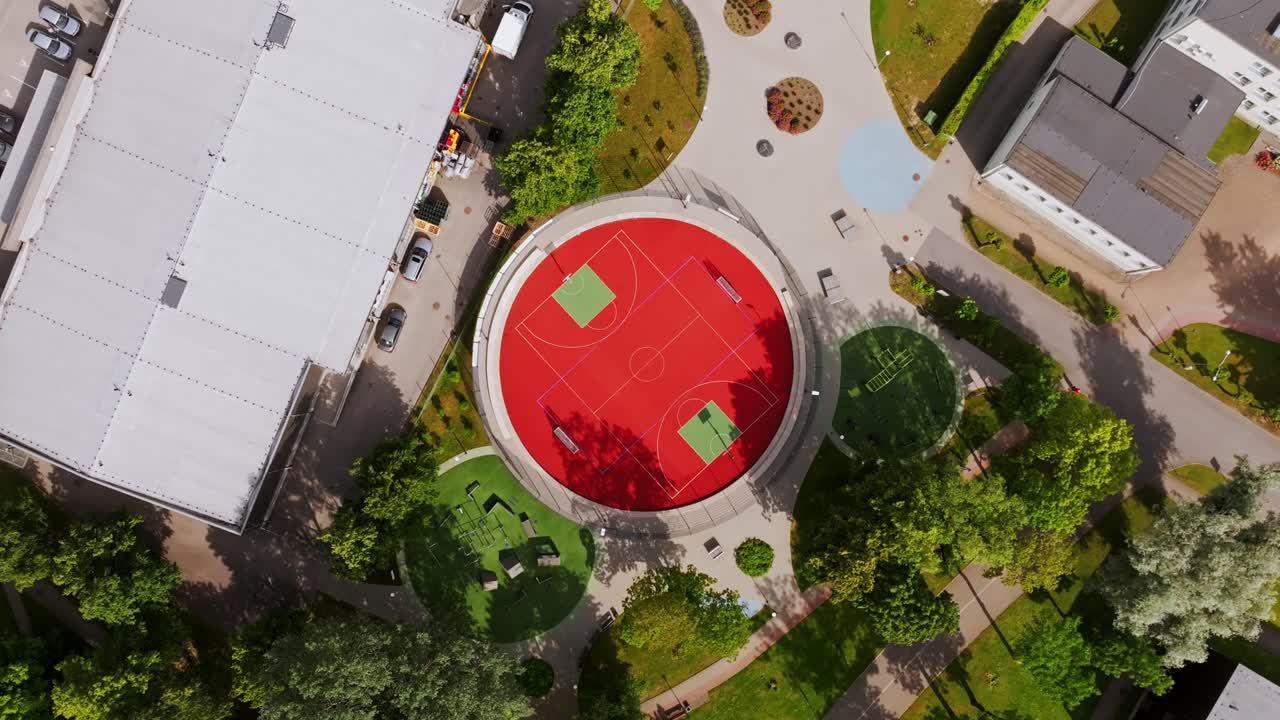 Drone spirals down over round court shaped like a giant red basketball, Dobele