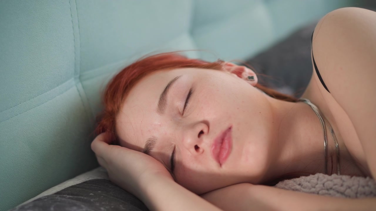 Rossa rilassata e assonnata. Studente a riposo in luce soffusa. Scena casuale di una rossa lentigginosa che si rilassa dopo lo studio. Studente dai capelli rossi pacifico sdraiato sul divano con una luce soffusa e accessori delicati.