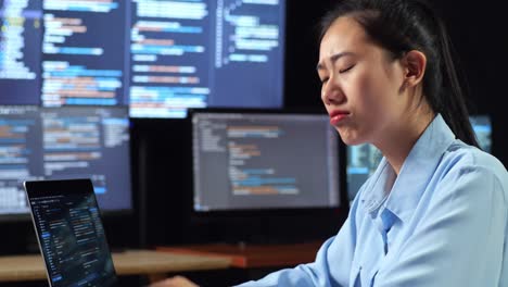 close up side view of asian female programmer thinking about something and raising his index finger while writing code by a laptop using multiple monitors showing database on desktops in the office