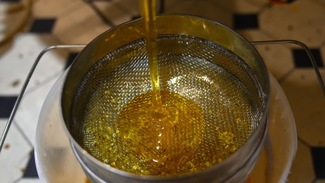 Metal sieve on top of the bucket for honey filtering. Fresh yellow liquid honey starts to flow from the machine. Healthy organic food concept.