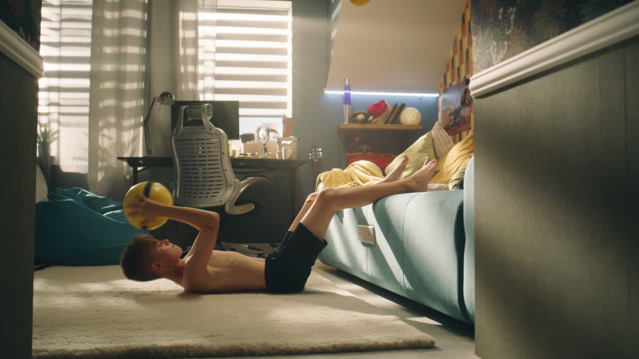Boy doing sit-ups in a bedroom with a ball