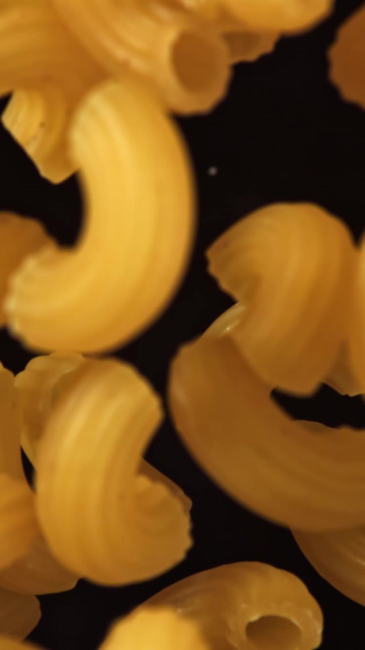 Scatto macro di pasta maccheroni dorata e secca su sfondo nero