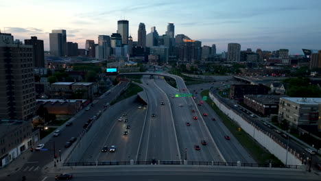 Antena-Crepuscular-Sobre-La-Autopista-Con-Tráfico-Hacia-El-Horizonte-De-La-Ciudad-De-Minneapolis