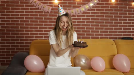 excited girl celebrates birthday online by webcam holding cake with candles