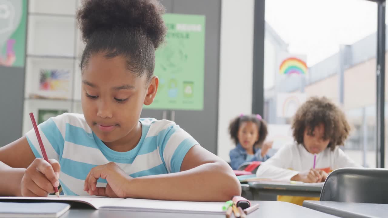 Video of biracial schoolgirl sitting at desk writing in school class