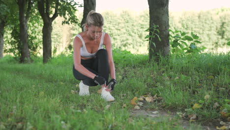 hermosa chica rubia trotando se ata los cordones de los zapatos y empieza a correr