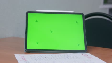 tablet pc negra con pantalla chromakey se encuentra en una mesa de madera en una hoja de papel con trabajo de prueba contra la pared gris en el aula de primer plano