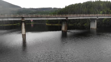 drone-shot-flying-under-steel-and-concrete-beam-bridge-over-the-Oasa-Lake,-Romania,-part-of-the-transalpine-highway