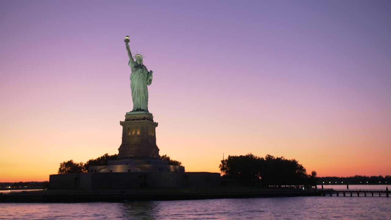 establishing shot of Statue of liberty silouhette at dawn, shot from a boat on orange and violet sky