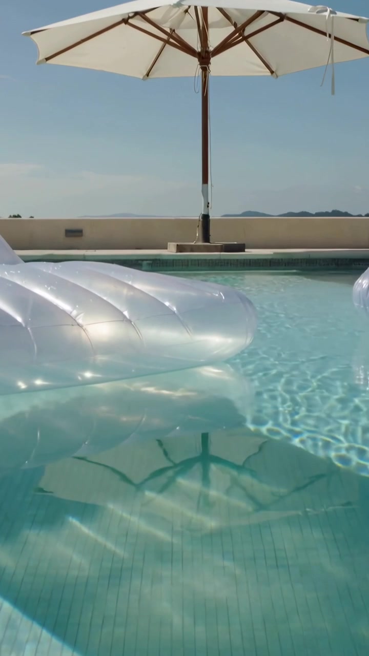 Vertical video: Light shifting, umbrella making rippled shadow on roof pool, two floats drifting