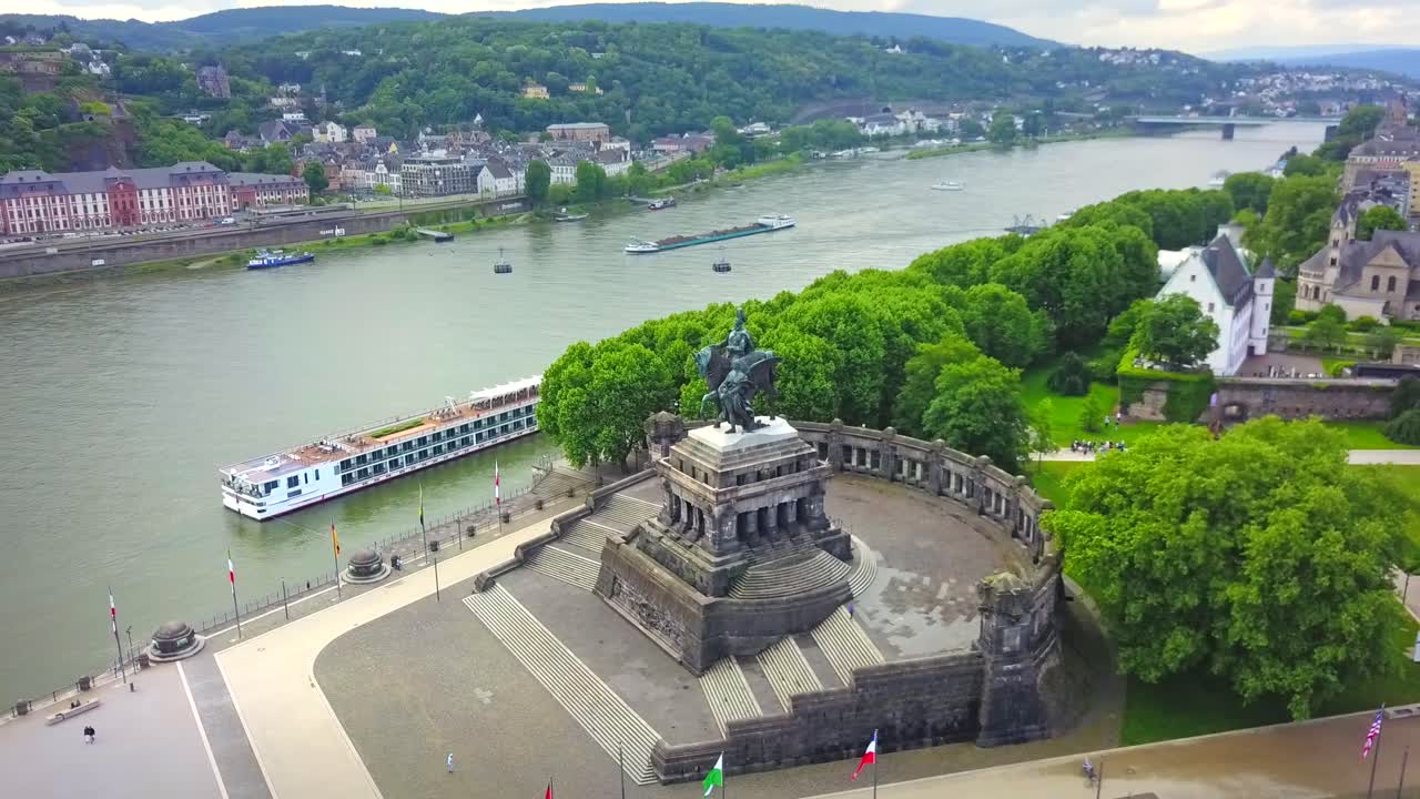 A stunning aerial shot of Deutsches Eck in Koblenz, Germany, where the Rhine and Moselle rivers meet. The monument, lush greenery, and historic cityscape create a breathtaking view.