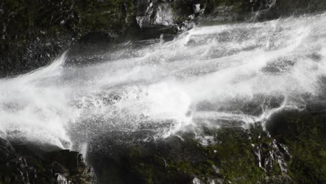 a vertical video of a waterfall over mossy rocks panning down