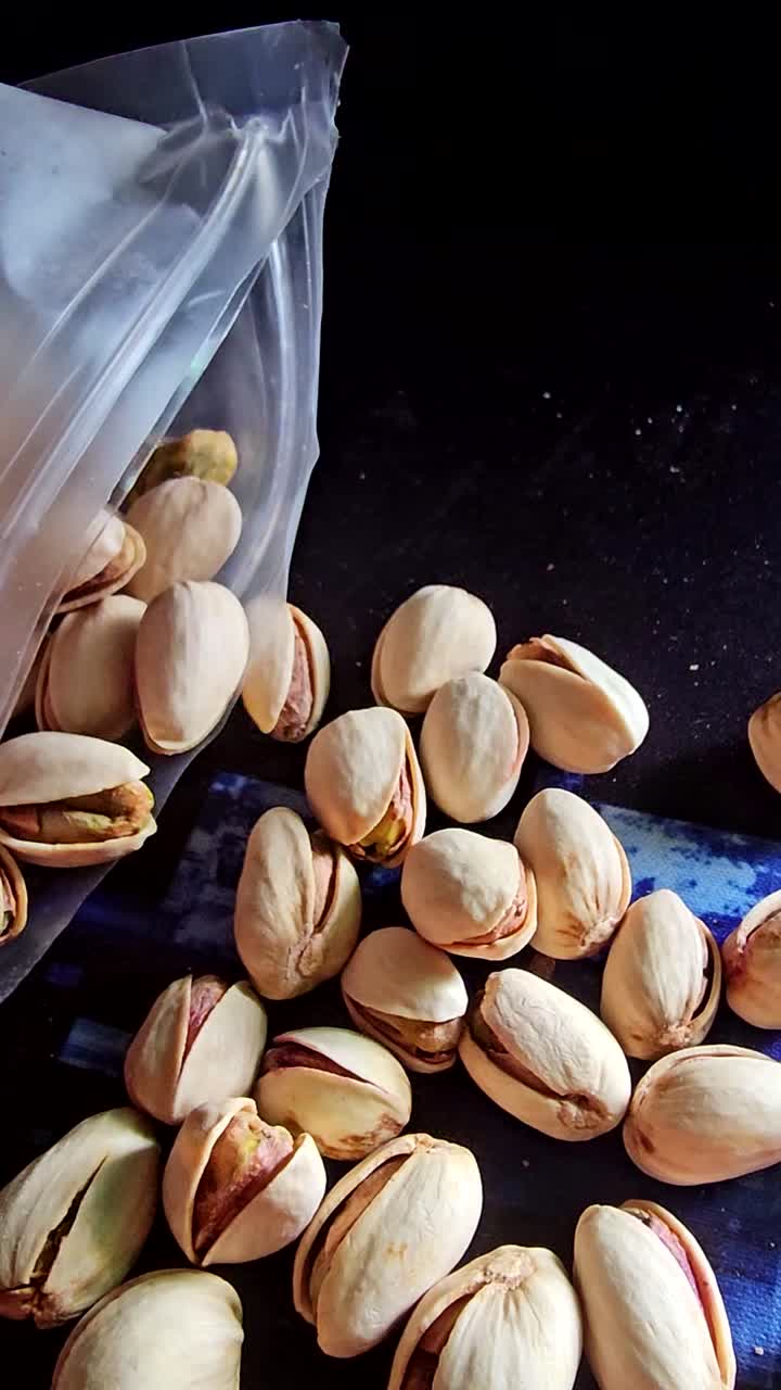 A close-up shot pistachio nuts spilling out of a transparent zip bag onto a dark surface