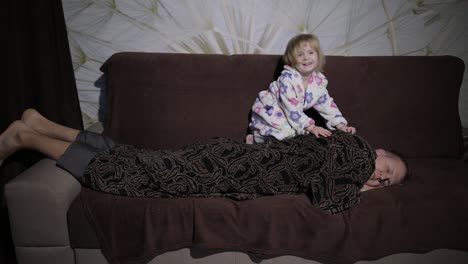 Little-girl-in-bathrobe-waking-her-father-up.-Man-sleeps-on-the-couch