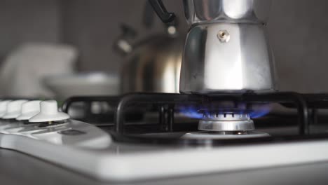 gas stove with blue flames and coffee in moka pot, turning on by hand, extreme closeup