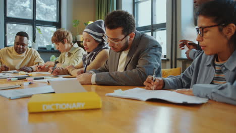 immigrant students writing in copybooks during lecture in language school