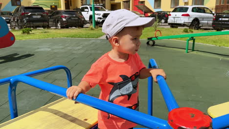 adorable caucasian kid in cap on the merry-go-round. smiling cute toddler on the playground in summer.