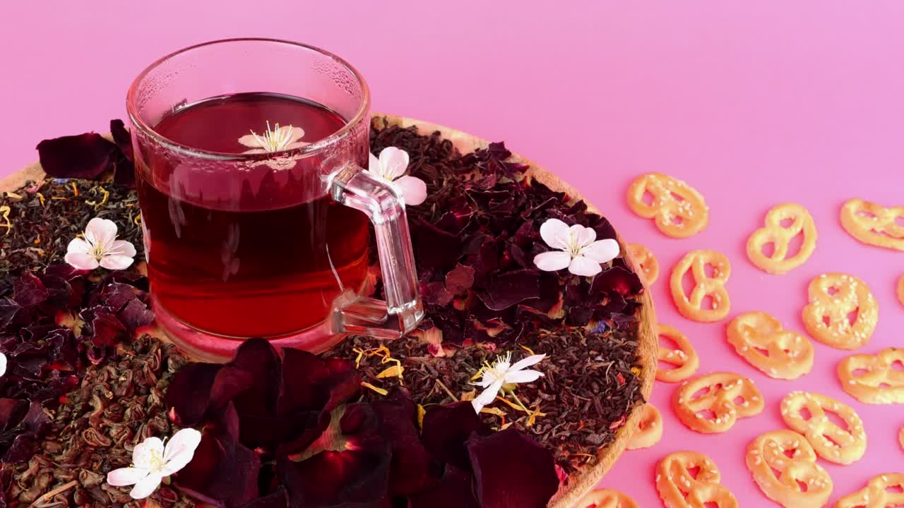 el té de flores en taza de vidrio gira lentamente en la iluminación rosada sobre un fondo rosado.