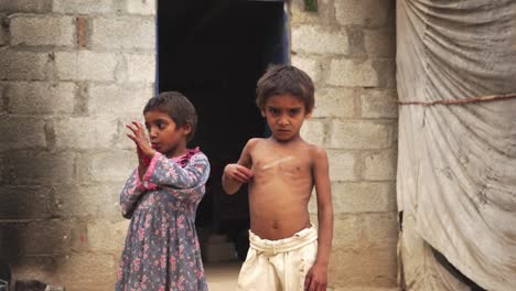 in front of their modest homes, children from a poor village are having their pictures taken, some not dressed neatly while others are wearing incomplete outfits.