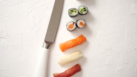 varios rollos de sushi con cuchillo japonés sobre fondo de pizarra de piedra blanca