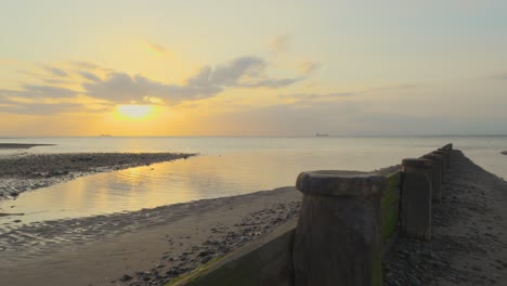 Pan-across-breakwater-with-ships-on-horizon-on-calm-sea-during-sunset-in-slow-motion-at-Fleetwood,-Lancashire,-UK