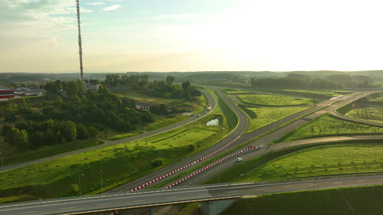 Wide aerial shot of a massive highway interchange near Gdynia featuring a communications mast on a hill, bathed in the golden glow of early morning light