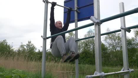 man doing leg pull ups on horizontal bar and flexing abdominal muscles outdoors - wide shot