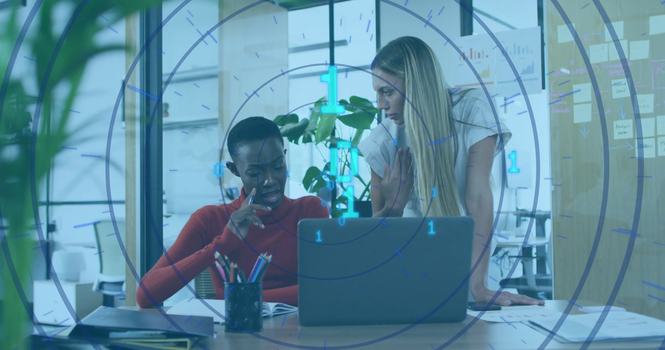 Seated woman pointing at laptop, standing woman leaning, reviewing business docs with cyan overlay