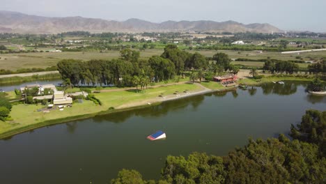 Drone-rises-above-trees-to-reveal-a-large-lake-or-lagoon-in-the-middle-of-green-agricultural-fields