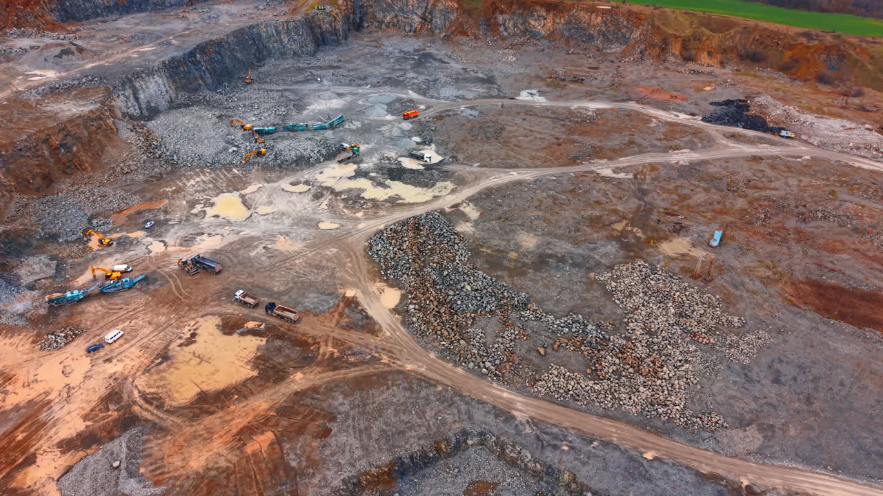 Aerial view of open pit granite quarry with industrial machinery. High angle shot showing excavators, trucks, and stone crushing equipment in a large active stone mine