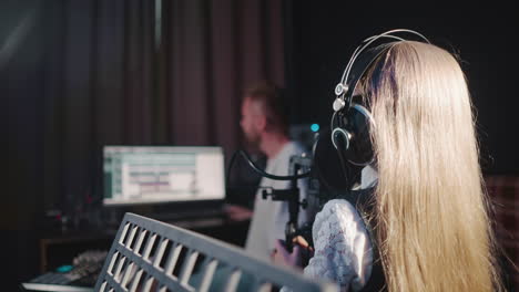 girl sings following teacher in audio studio. vocal teacher controls girl in headphones singing. talented child prepares for performing in studio