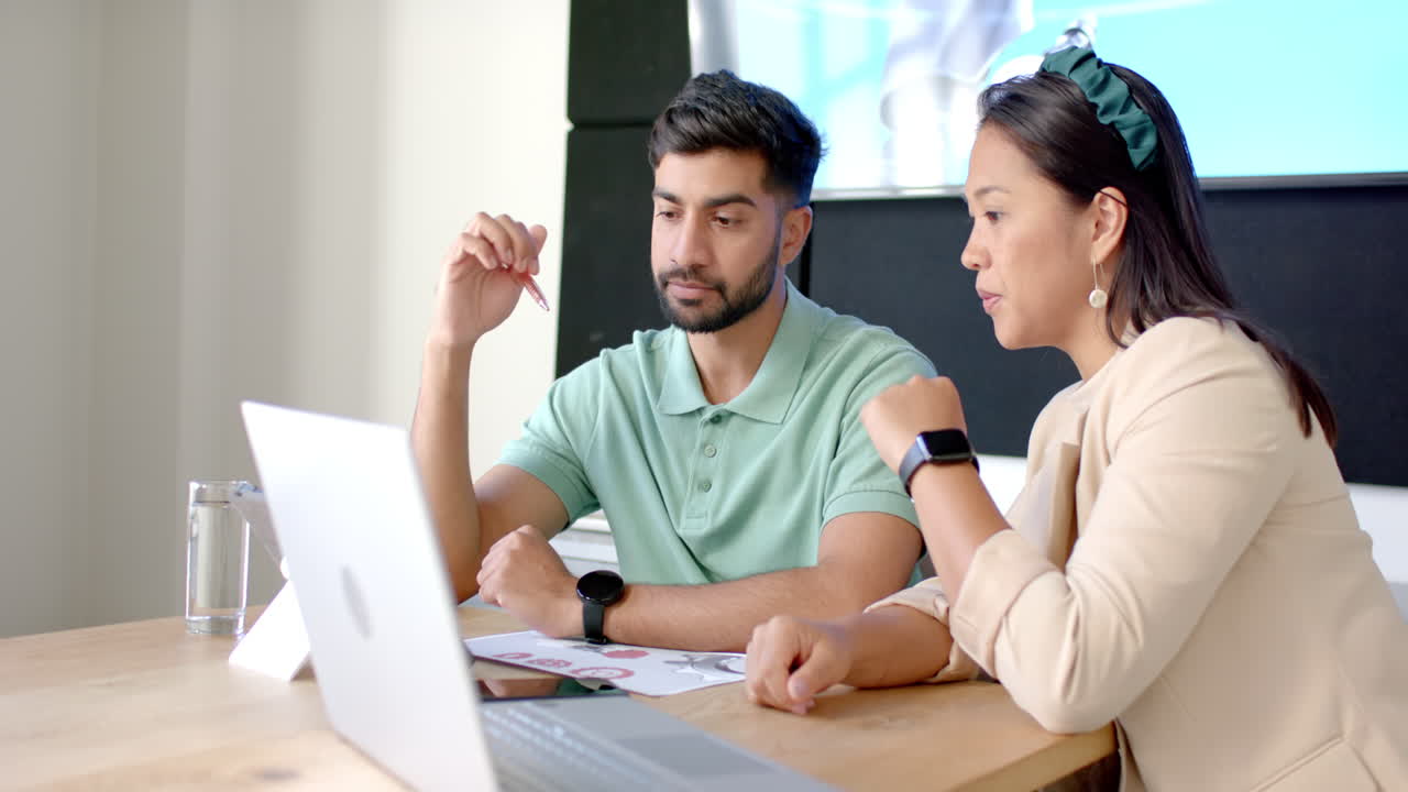 Collaborating on project, colleagues discussing ideas while using laptop in office