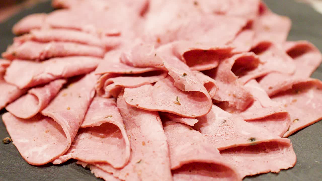 Primo piano di fette di roast beef condito disposte su ardesia, con una forchetta che ne solleva una.