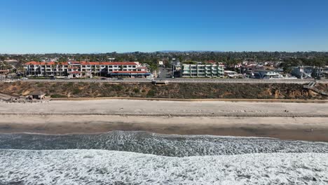 aerial backward moving shot over the pacific ocean with the view of the sandy beach and the town of carlsbad california, usa with waves crashing on the beach