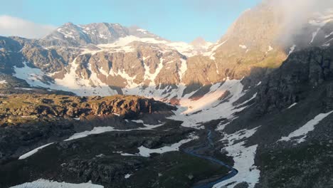 aerial: flying over alpine valley at sunrise, high altitude mountain range