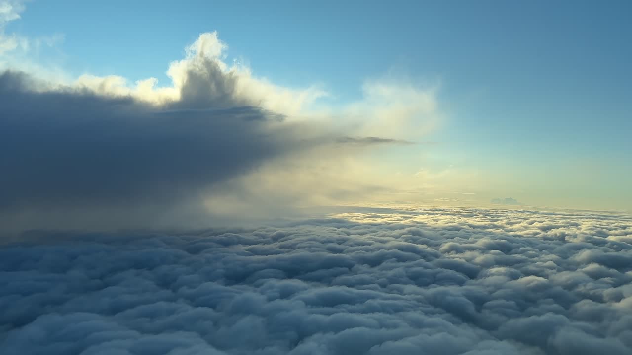An aerial view taken from inside a jet cockpit flying over an endless sea of clouds, with a storm cloud on the left. Scene Illuminated by the warm sunrise light.
