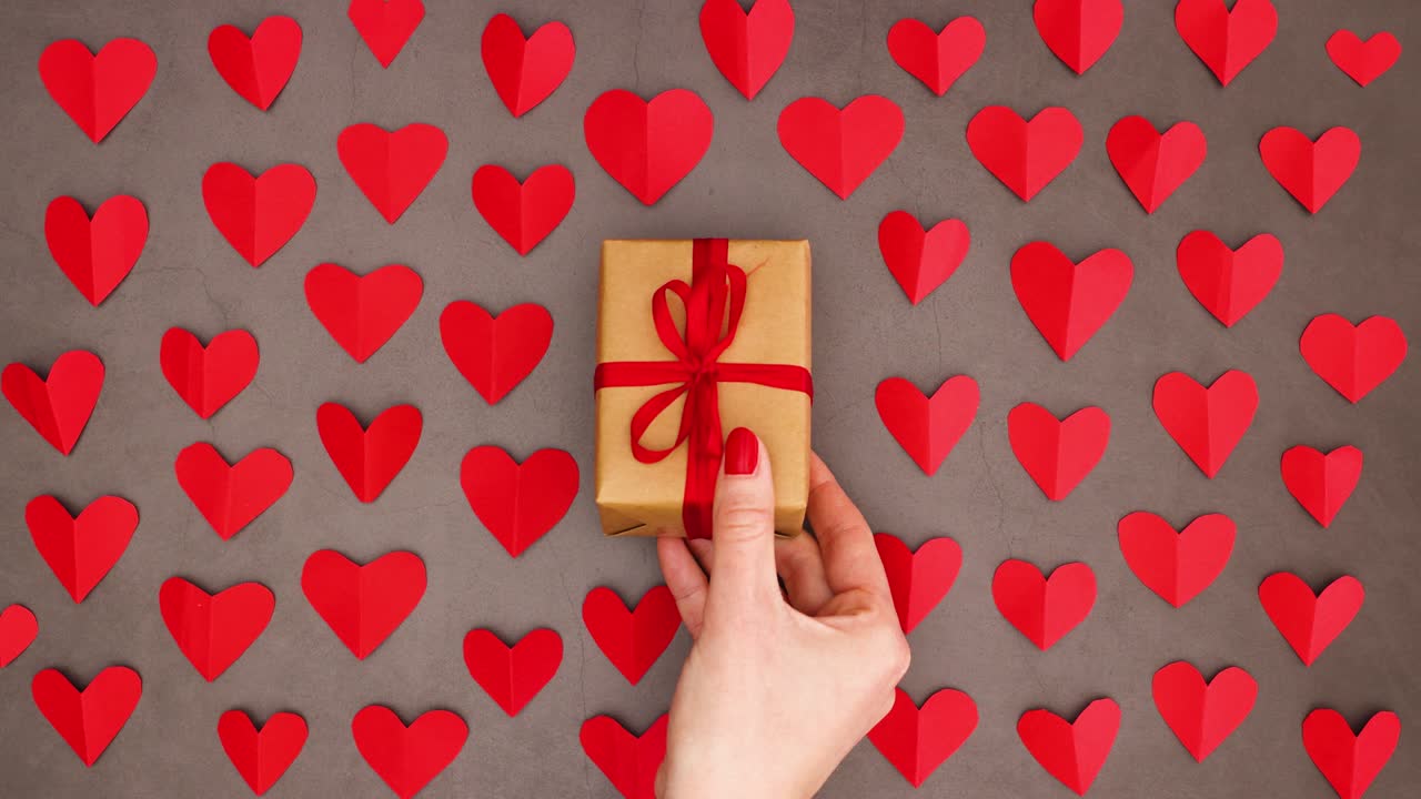 la mujer puso a mano una caja de regalos con cinta roja para san valentín en la mesa con corazones rojos - detenga el movimiento