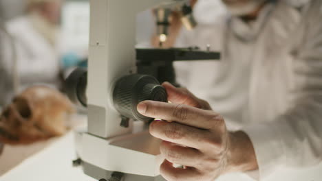 Close-Up of Archaeologist Adjusting Microscope Focus in Research Laboratory