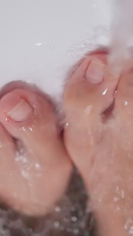 tap water runs on woman feet in bathtub closeup. lady enjoys foamy bath with hot water in cozy bathroom closeup. body care hygiene and massage