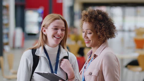 Female-College-Student-Meeting-With-Woman-Tutor-In-Busy-Communal-Campus-Building