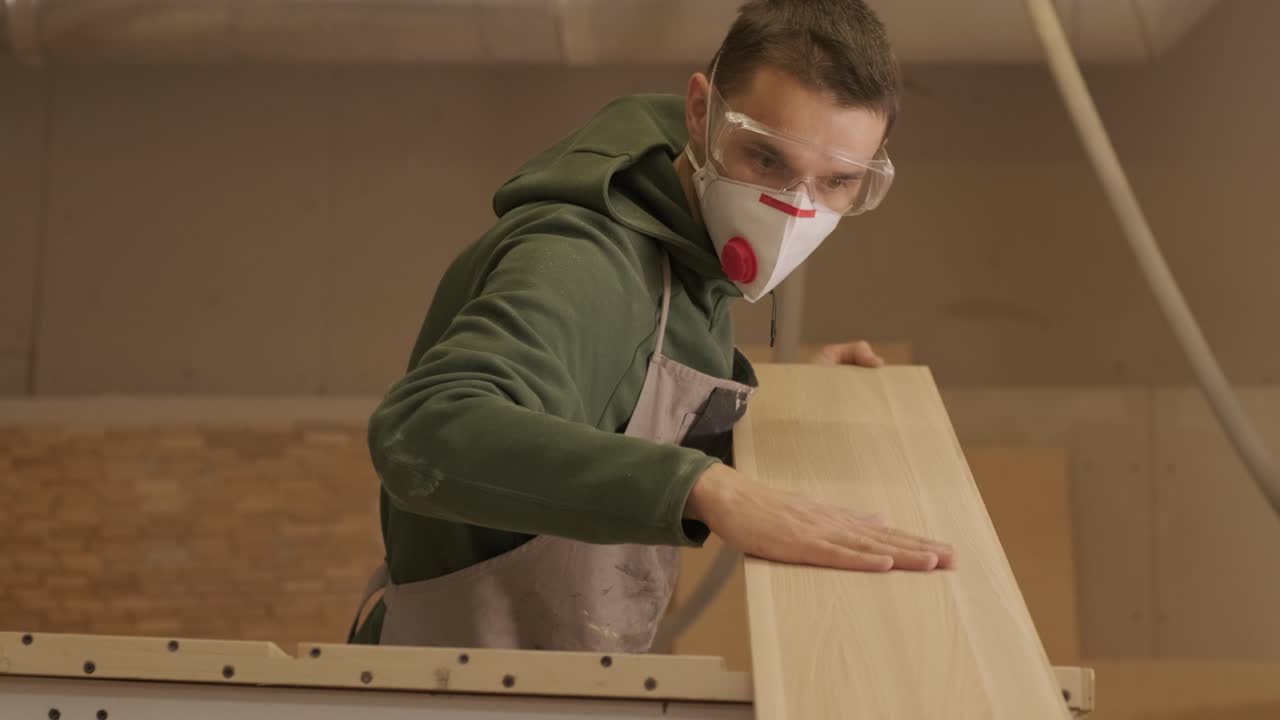 trabajador de la madera profesional en máscara y gafas comprueba la madera en bruto, tabla de madera, panel de contrachapado