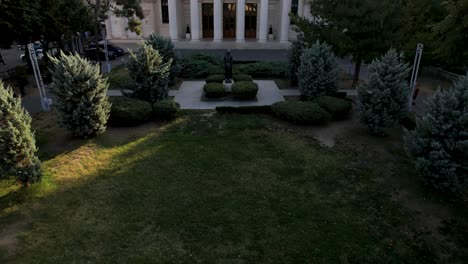 Slow-Aerial-Reveal-Of-The-Romanian-Athenaeum-At-Sunrise-In-Bucharest-With-A-Beautiful-Green-Garden-In-The-Foreground