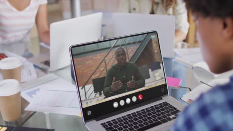 mujer afroamericana usando una computadora portátil para una llamada de video, con un colega de negocios en la pantalla
