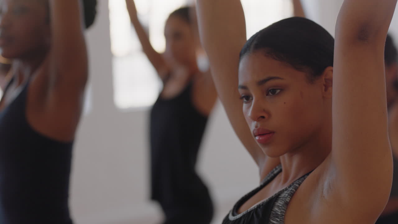 linda mulher de ioga de raça mista praticando meditação em pose de guerreiro com um grupo de mulheres multirraciais desfrutando de um estilo de vida saudável, exercitando-se no estúdio de fitness ao nascer do sol