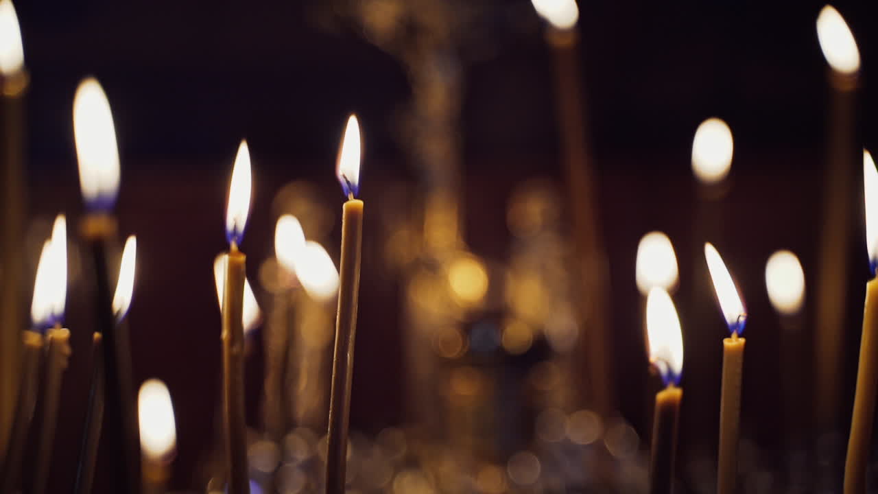Many candles burning in the night temple. Abstract candles background. Yellow candle flames glowing on blur dark background in church.