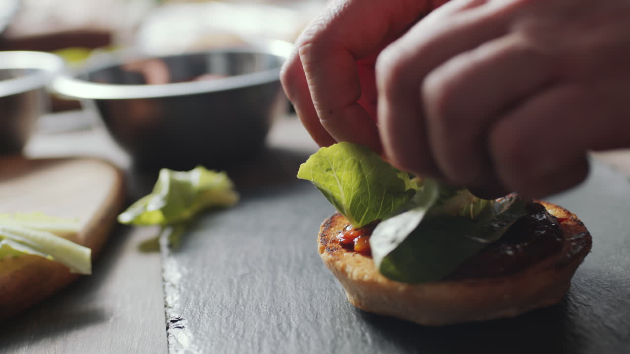 añadiendo lechuga al pan de hamburguesa con salsa