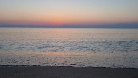 calm water surface and sea waves splash on sandy beach before sunrise