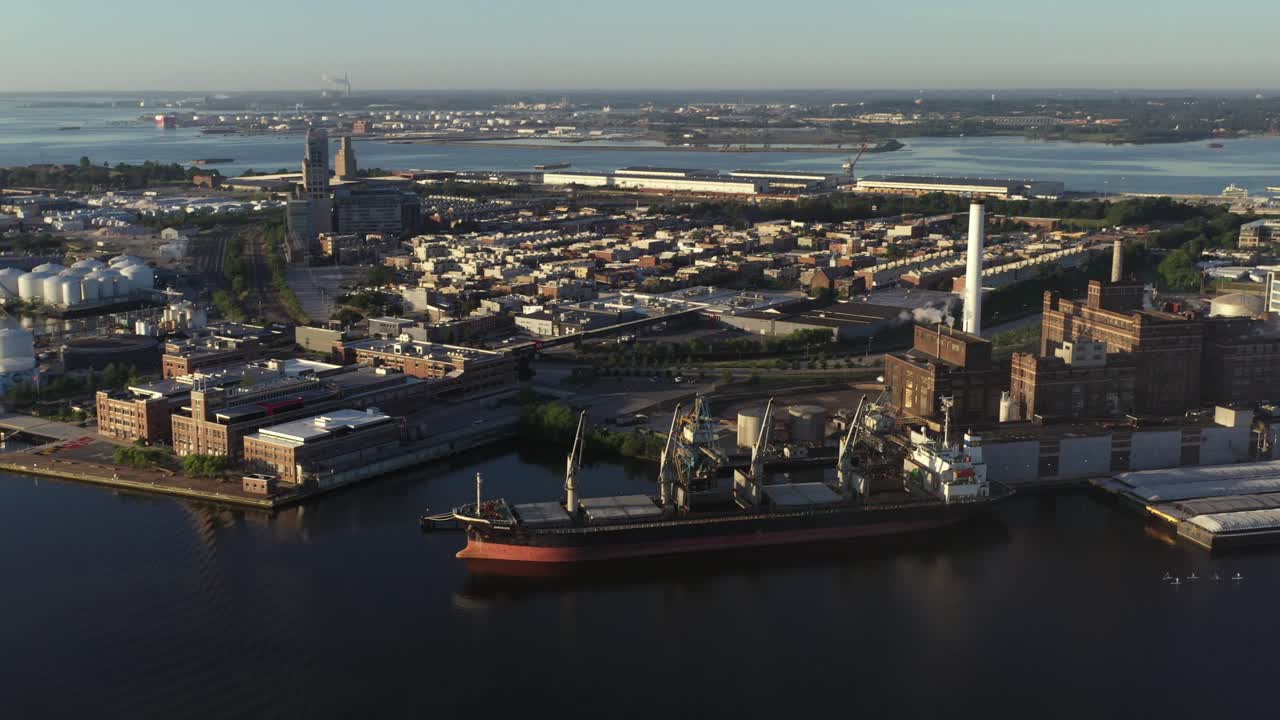 Aerial tilting up pan across industrial harbor in Baltimore Maryland at golden hour sunrise